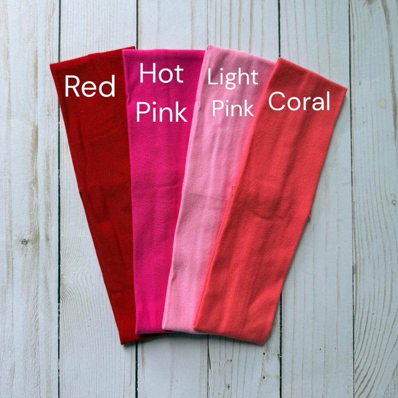 Puede incluir: Cuatro diademas rectangulares de tela dispuestas una al lado de la otra en rojo, rosa intenso, rosa claro y coral. Cada diadema presenta el nombre de su color impreso en texto blanco directamente sobre la tela para una identificaci&oacute;n clara.