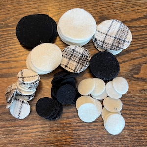May include: Assortment of felt circles in black, white, and black and white plaid patterns. The circles are various sizes and are stacked in piles.