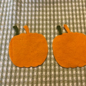 May include: Two felt orange pumpkins with green stems on a white and green checkered background.