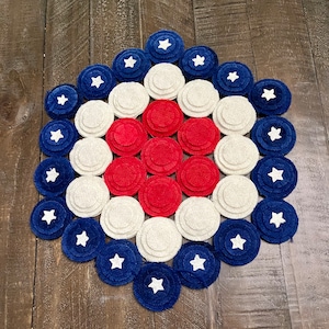 May include: A red, white, and blue felt circle rug with a concentric circle design. The circles are arranged in a pattern of red, white, and blue, with a white star in the center of each circle.