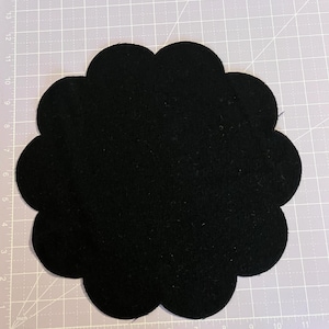 May include: Black felt circle with a scalloped edge. The circle is approximately 8 inches in diameter.
