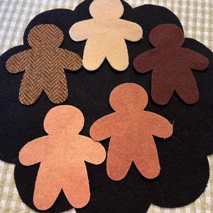 May include: Five felt gingerbread people in different colors and patterns. The gingerbread people are arranged in a circle on a black felt background.