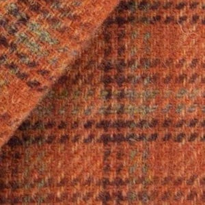 May include: Close-up of a textured orange fabric with a plaid pattern. The fabric has a woven appearance with flecks of green and dark brown throughout. The material appears to be thick and possibly wool or a wool blend.