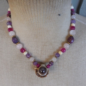 May include: A necklace made with pink, white and purple beads with a pendant made from a deer antler with a purple stone in the centre.