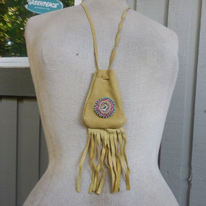May include: A tan leather pouch with a beaded circle design and fringe. The pouch is hanging from a tan leather cord.