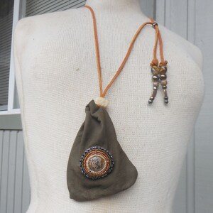 May include: A brown leather pouch with a beaded circle design hangs from a brown leather cord with brown and gold beads.