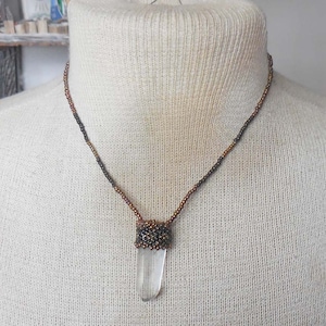 Peut inclure: Un collier avec un pendentif en cristal de quartz transparent et une chaîne en cuivre et noir perlée.