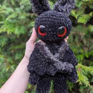 Puede incluir: Juguete de peluche negro de crochet con grandes ojos rojos y alas peludas. El juguete está hecho de hilo suave y tiene un aspecto caprichoso y de dibujos animados.