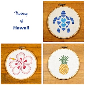 May include: Four embroidery hoops with different Hawaiian-themed designs: a blue sea turtle, a pink hibiscus flower, a yellow pineapple, and the text "Thinking of Hawaii".
