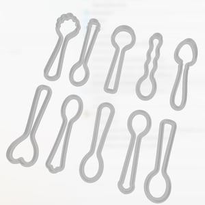 Op de afbeelding: Een set van negen lichtgrijze plastic koekjesvormpjes, elk in de vorm van een andere stijl lepel of keukengerei. De collectie bevat diverse handvatontwerpen en lepelvormen, gerangschikt in twee rijen tegen een witte achtergrond.