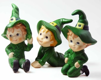 Seated Baby Green Elf Pixie Leprechaun Figurine Holding Shamrocks Clovers Peapod Green Suit Flower Hat Brown Hair Japan 1970s