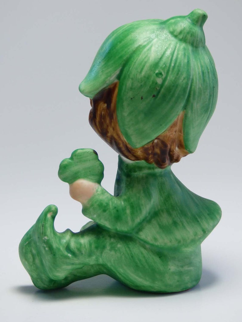 Seated Baby Green Elf Pixie Leprechaun Figurine Holding Shamrocks Clovers Peapod Green Suit Flower Hat Brown Hair Japan 1970s