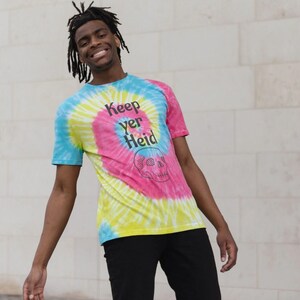 以下が含まれることがあります： スカルのグラフィックと「Keep yer Heid」という黒いテキストが入ったタイダイTシャツです。