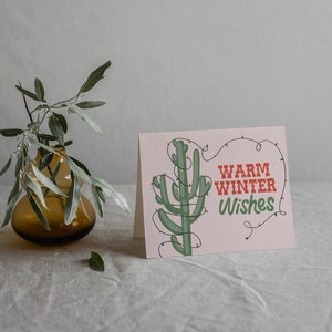 Cálidos deseos de invierno, tarjeta navideña, tarjeta festiva, cactus navideño, luces navideñas, tarjeta con un juego de palabras