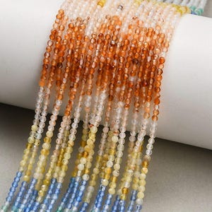 May include: Multiple strands of small, faceted, round beads arranged in a vertical gradient pattern. The colors transition from deep orange and amber at the top, fading into pale yellow, and ending with light blue and green tones at the bottom.