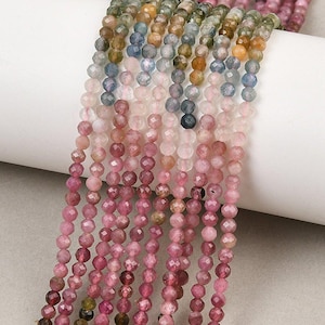 May include: Multiple strands of faceted, round gemstone beads in a gradient of colors. The beads transition from deep pink and magenta at the bottom to lighter pink, blue, green, and yellow tones toward the top, creating a vibrant, multi-colored display.