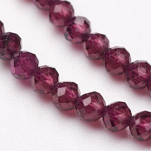 Peut inclure: Gros plan sur deux rangées de perles violet foncé à facettes. Les perles ont une surface à facettes multiples qui capte la lumière, créant un effet scintillant. Les perles sont enfilées, suggérant qu'elles sont destinées à la fabrication de bijoux ou à l'artisanat.