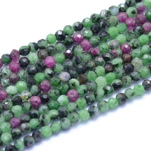 Peut inclure: Gros plan sur une collection de perles de pierres précieuses facettées. Les perles sont un mélange de couleurs vertes, vert foncé et magenta. Les perles sont rondes et semblent être enfilées, adaptées à la fabrication de bijoux.