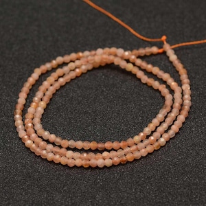 May include: Several strands of small, faceted, peach-coloured gemstone beads. The beads are strung on an orange thread, creating a delicate look. These beads are likely for jewellery making.
