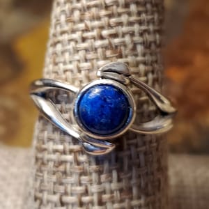 Könnte beinhalten: Ein silberner Ring mit einem blauen Lapislazuli-Stein, der in einem einzigartigen, abstrakten Design gefasst ist.