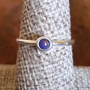 Puede incluir: Un anillo de plata con una pequeña piedra preciosa redonda azul engastada en el centro.