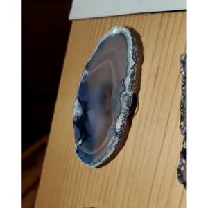 May include: A blue and white agate slice with a natural edge, mounted on a metal base. The agate has a unique pattern of swirls and bands.