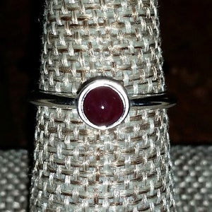 May include: A silver ring with a dark red gemstone set in a bezel setting.