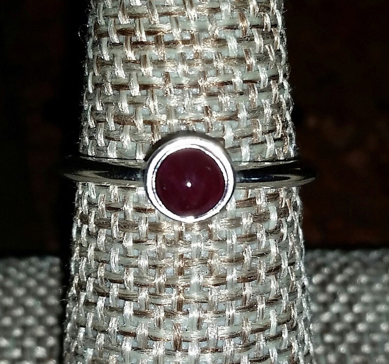 May include: A silver ring with a dark red gemstone set in a bezel setting.