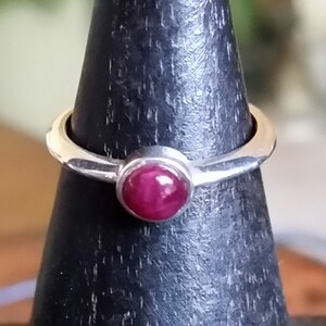 May include: A silver ring with a deep red gemstone set in a bezel setting.