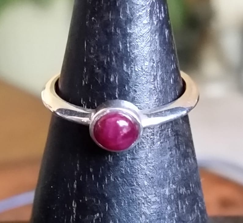 May include: A silver ring with a deep red gemstone set in a bezel setting.