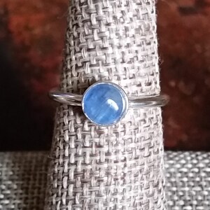 Puede incluir: Un anillo de plata con una piedra preciosa azul claro. El anillo está en un expositor.