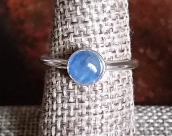 May include: A silver ring with a light blue gemstone. The ring is on a display stand.