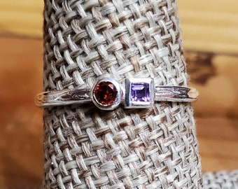 May include: A silver ring with a round orange gemstone and a square purple gemstone.