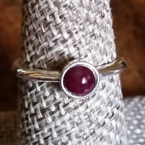 May include: A silver ring with a deep red gemstone set in a bezel setting.