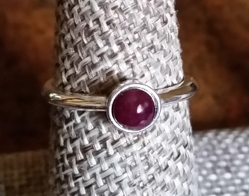 May include: A silver ring with a deep red gemstone set in a bezel setting.