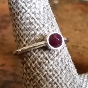 May include: A silver ring with a round, deep red gemstone set in a bezel setting.