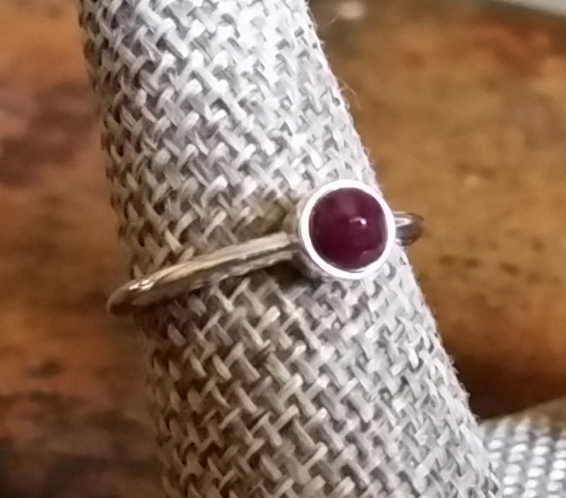 May include: A silver ring with a round, deep red gemstone set in a bezel setting.