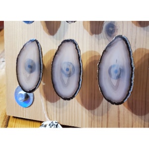 May include: Three agate knobs with a white and gray pattern and a dark brown border. The knobs are mounted on a wooden surface.