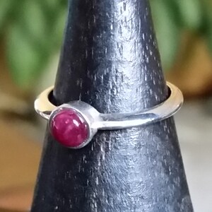 May include: A silver ring with a round, deep red gemstone set in a bezel setting.