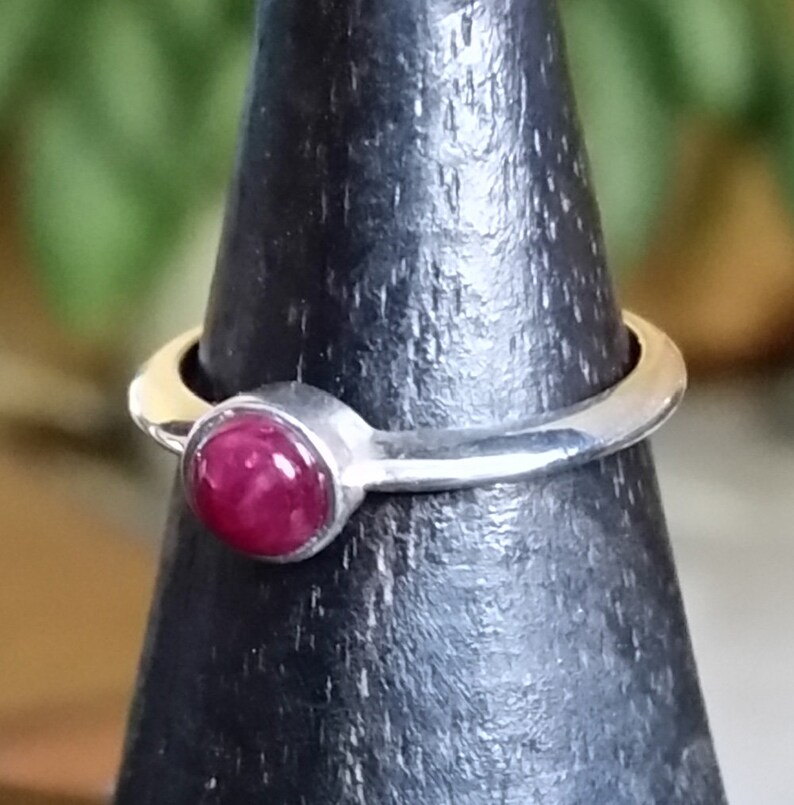 May include: A silver ring with a round, deep red gemstone set in a bezel setting.