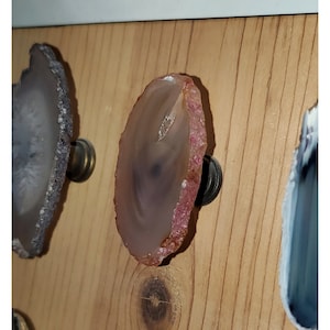 Peut inclure: Une tranche d'agate rose et blanche avec un bord naturel, montée sur un bouton en métal. Le bouton est fixé à une surface en bois.