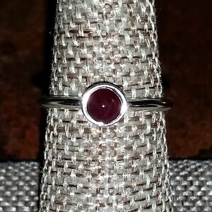 May include: A silver ring with a dark red gemstone set in a bezel setting.
