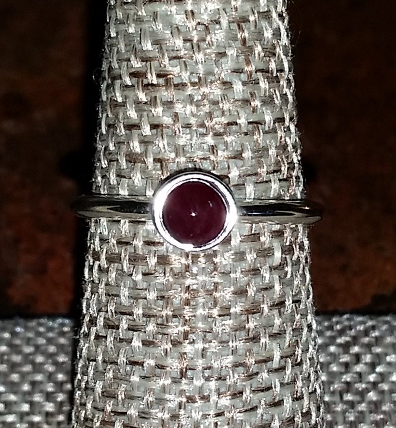 May include: A silver ring with a dark red gemstone set in a bezel setting.