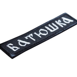 May include: Black embroidered patch with white lettering that reads "БАТЮШКА".