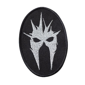 Puede incluir: Parche bordado negro con un diseño blanco de una cara estilizada con una corona de púas.