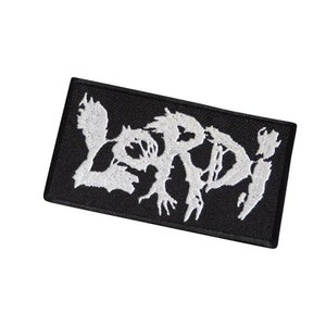 Könnte beinhalten: Schwarzer gestickter Patch mit dem Wort "LORD" in weißen Buchstaben. Die Buchstaben sind stilisiert und haben einen gezackten, abgenutzten Look.