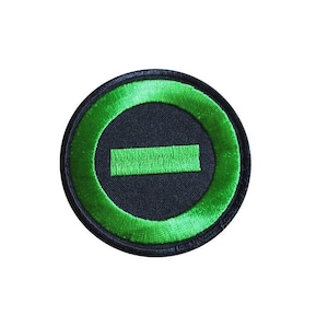 Può includere: Una toppa ricamata verde e nera con un cerchio e una linea orizzontale al centro.