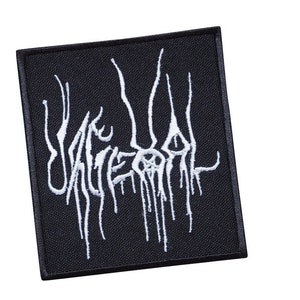 Op de afbeelding: Zwarte geborduurde patch met witte tekst die "UNREAL" luidt. De tekst is gestileerd en lijkt te druppelen.