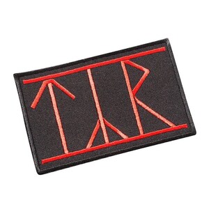 May include: Black rectangular patch with red embroidered stylized letters and lines. The patch has a red border. The letters appear to be a stylized version of the letters T, L, and R. The patch is on a white background.