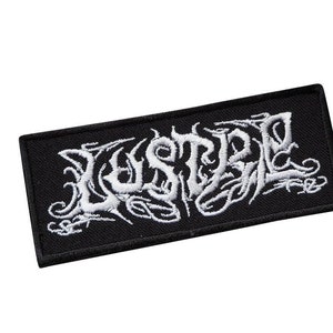 Op de afbeelding: Zwarte geborduurde patch met het woord "LESTRAL" in witte cursieve letters.